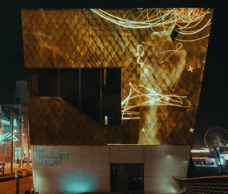 Lighting display of wiggly light lines and a large hand reaching up projected on the side of a building